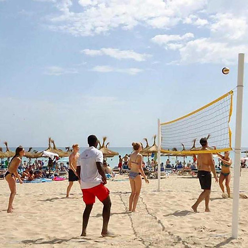 Jóvenes jugando voleibol en la playa del hotel Playa Esperanza Resort con sombrillas y el mar de fondo.