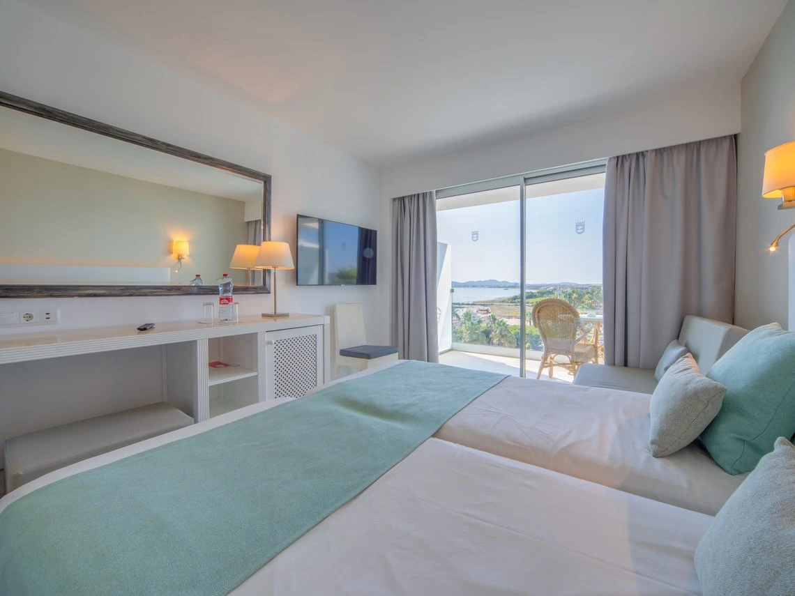 Habitación luminosa con dos camas, espejo grande y balcón con vista al mar. Playa Esperanza Resort
