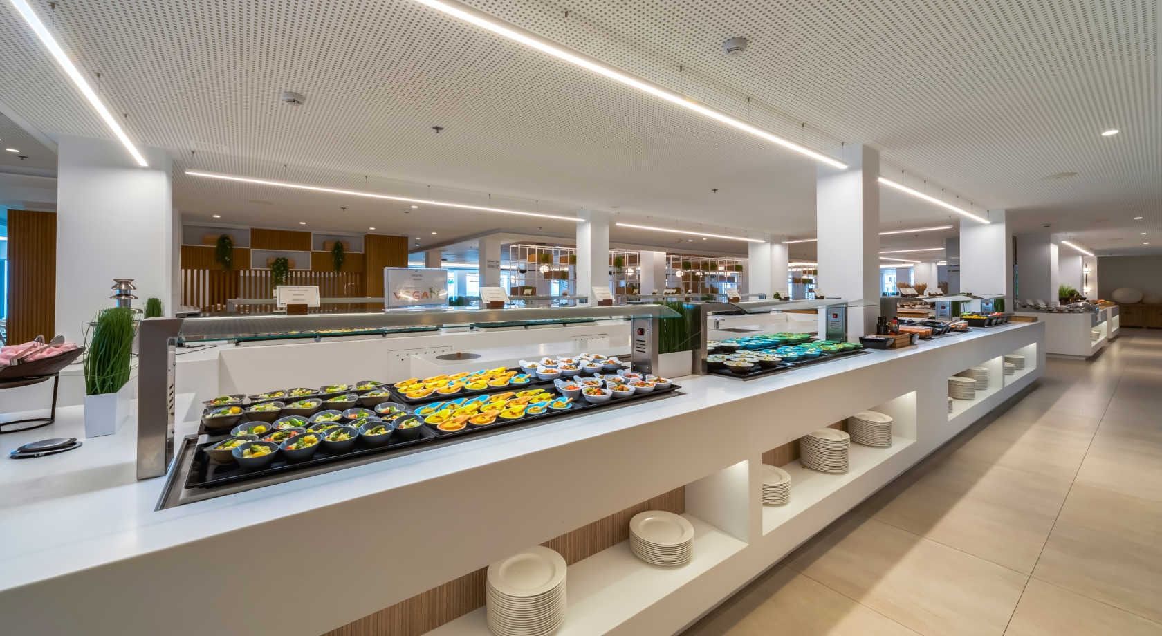 Buffet de desayuno en hotel, con mesas de comida y Playa Esperanza Resort, iluminación moderna y decoración elegante.