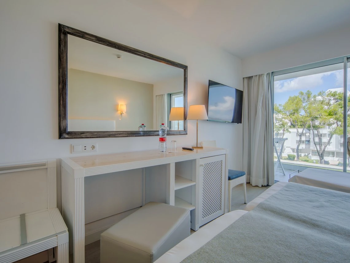 Habitación de hotel moderna con espejo grande, tocador, dos camas y vistas al exterior. Playa Esperanza Resort