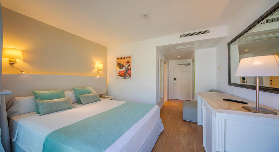 Habitación moderna con cama doble, lámparas de pared y un gran espejo. Playa Esperanza Resort