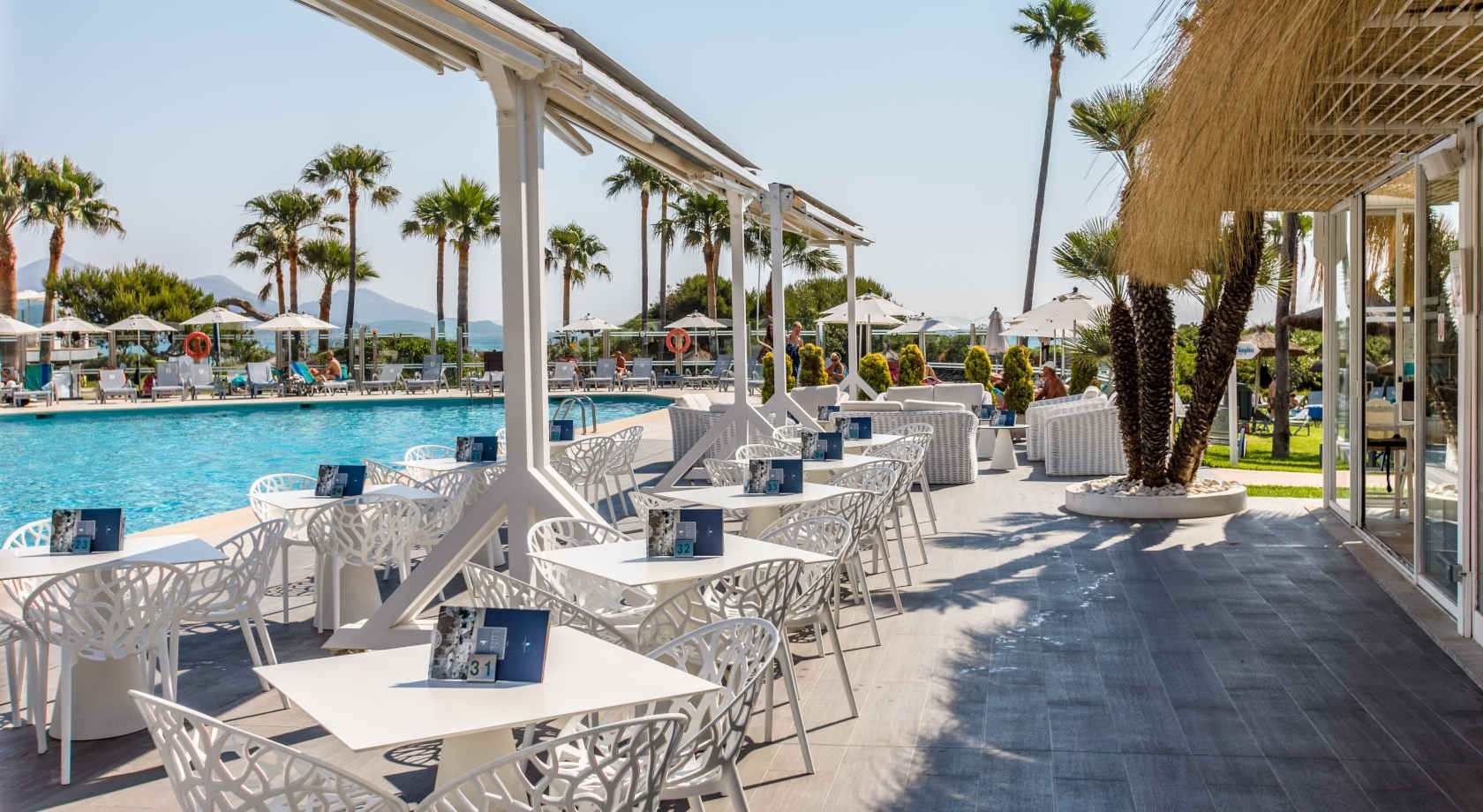 Terraza de restaurante con vistas a piscina y palmeras. Playa Esperanza Resort en Mallorca.