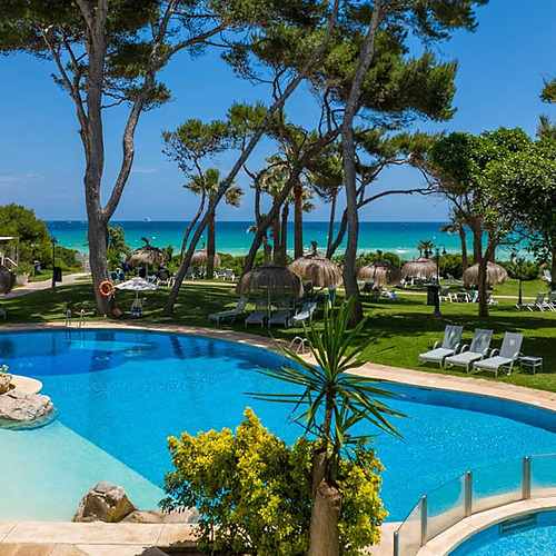 Piscina de hotel con palmeras, césped y mar turquesa. Playa Esperanza Resort ideal.