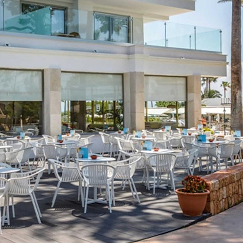 Terraza de restaurante con mesas y sillas blancas, palmeras y Playa Esperanza Resort.