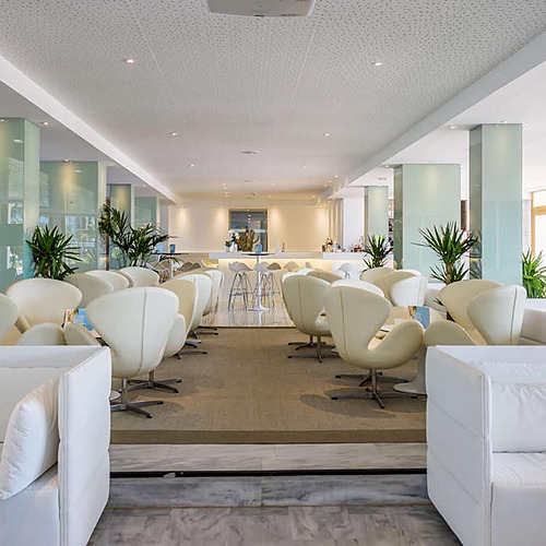 Sofisticado lobby de hotel con asientos blancos, plantas y barra Playa Esperanza Resort.