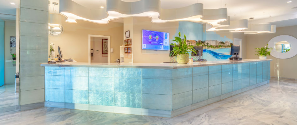 Recepción moderna de hotel con decoración náutica y pantalla de TV Playa Esperanza Resort.