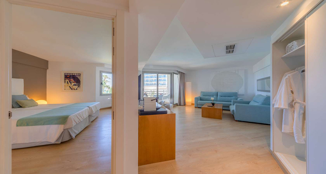 Suite moderna con cama, sala de estar azul y armario, ideal para tu Playa Esperanza Resort.