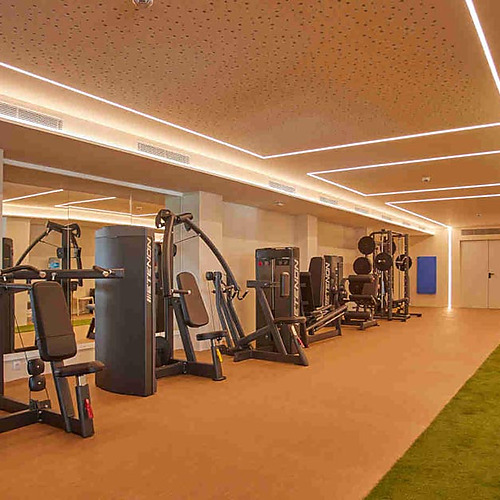 Gimnasio moderno con máquinas de pesas, área de césped artificial y luz ambiental. Playa Esperanza Resort perfecto para entrenar.
