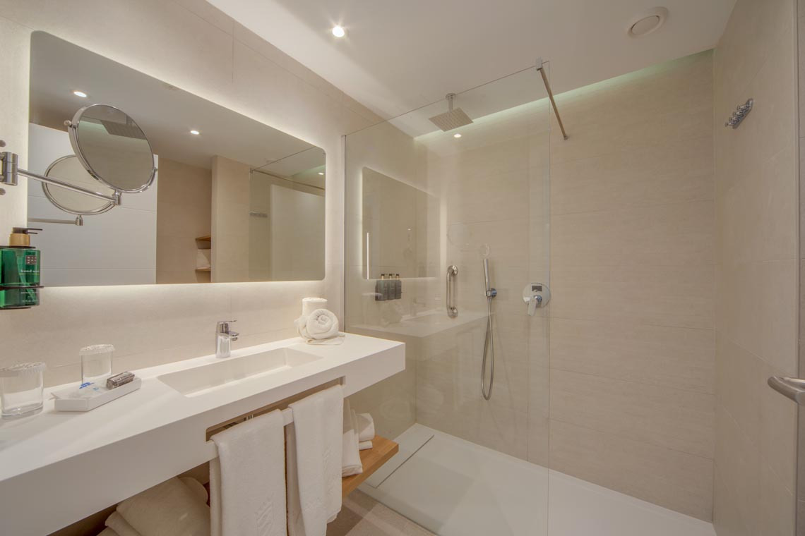 Baño moderno con ducha de cristal, lavabo y espejo iluminado para tu Playa Esperanza Resort.