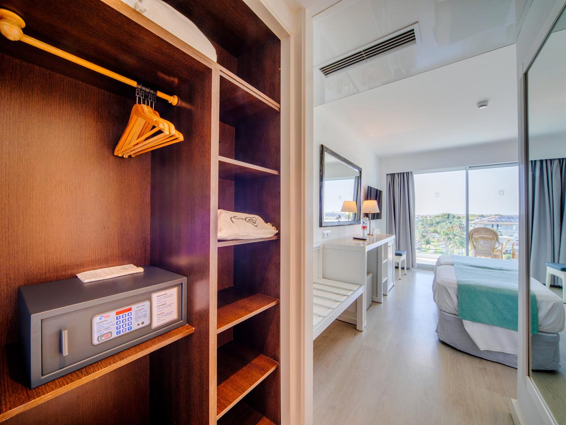 Armario de hotel con caja fuerte, perchas y vista a la habitación y al balcón con Playa Esperanza Resort.