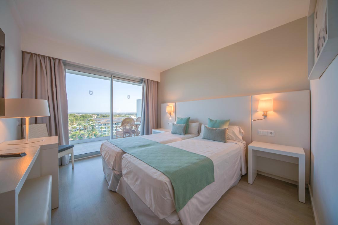 Habitación de hotel con dos camas, balcón y vista al mar, perfecta para tu Playa Esperanza Resort.