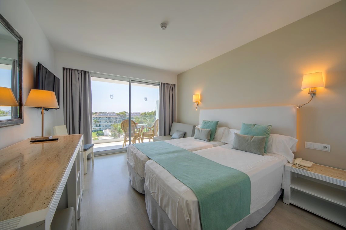 Habitación de hotel con dos camas, balcón y vista exterior, perfecta para tu Playa Esperanza Resort.