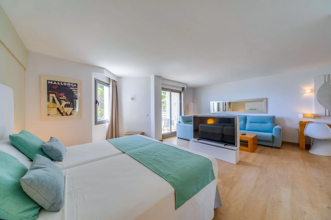 Habitación de hotel luminosa con cama doble, sofá azul, TV y póster de Playa Esperanza Resort.