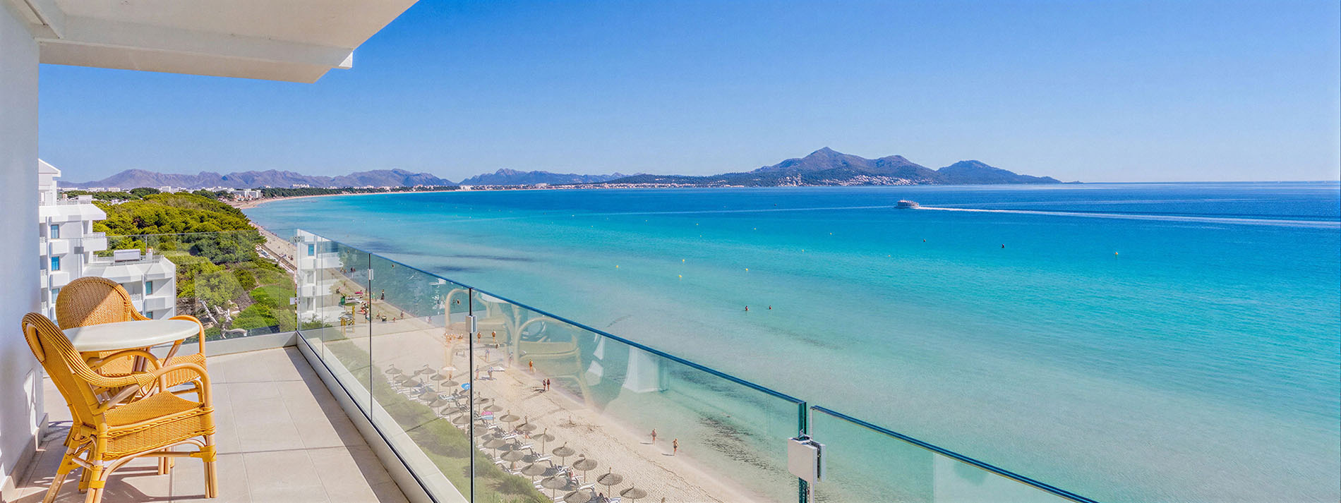 Terraza con vista al mar enPlaya Esperanza Resort. Sillas de mimbre y mesa junto a la playa turquesa.
