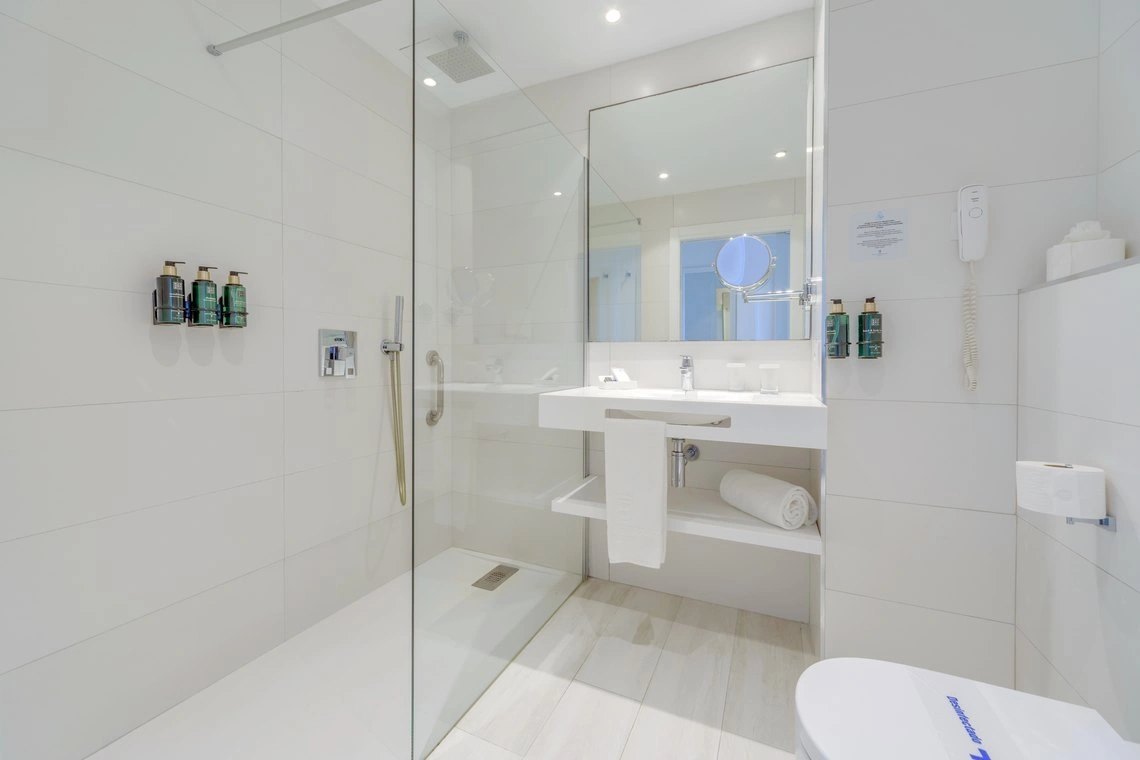 Baño moderno con ducha y lavabo, espejo con aumento. Playa Esperanza Resort para su comodidad.