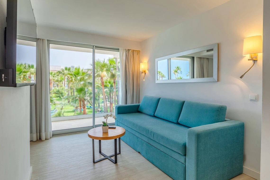 Amplia habitación con sofá turquesa y vista a palmeras Playa Esperanza Resort.