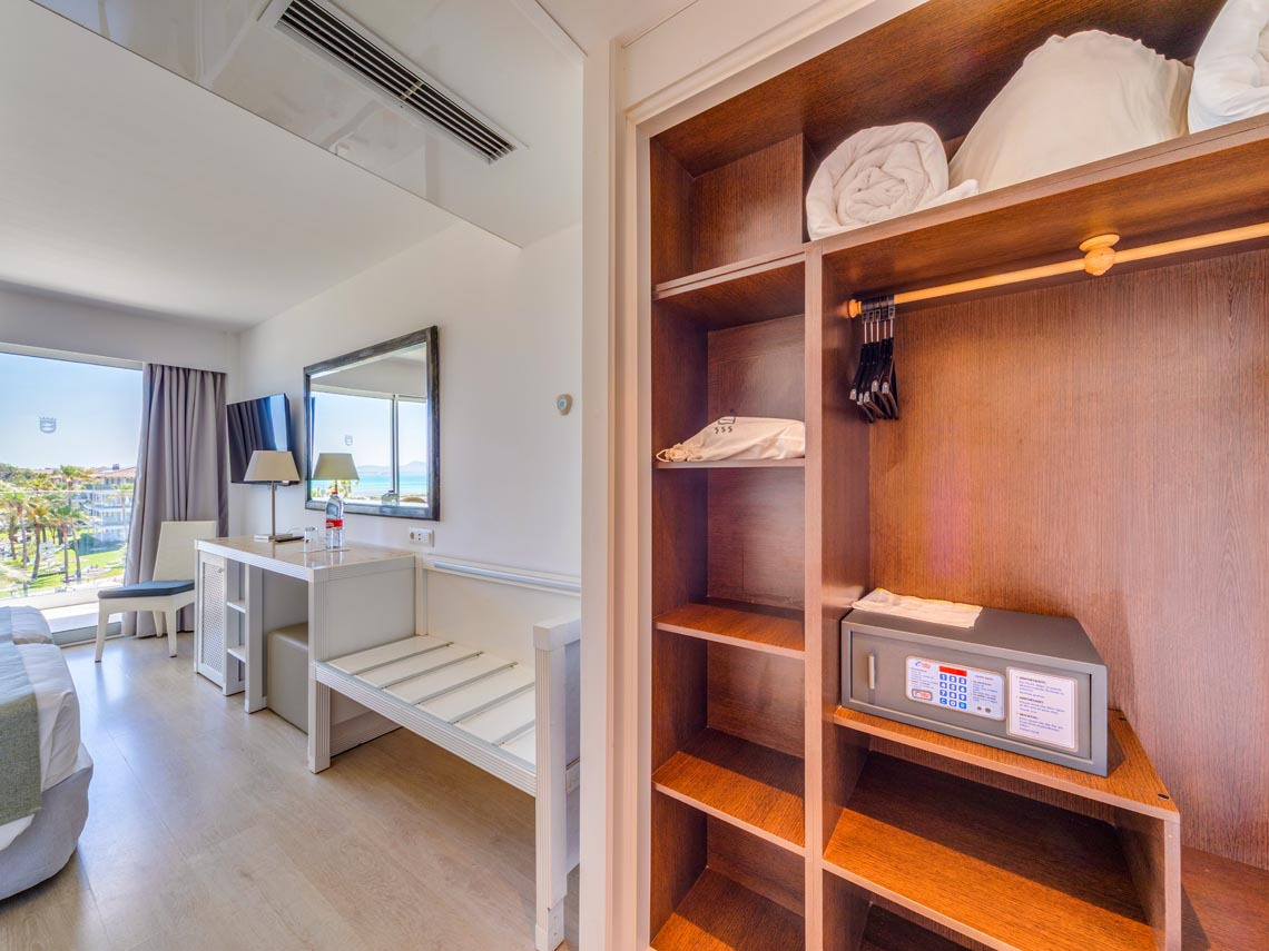 Armario de hotel con caja fuerte, toallas y perchas, cerca de una ventana con vistas Playa Esperanza Resort.