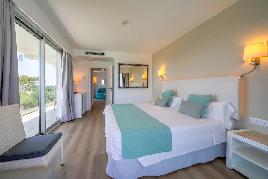 Habitación luminosa con cama doble, decorada en tonos turquesa y grises, con vistas a un balcón. Playa Esperanza Resort