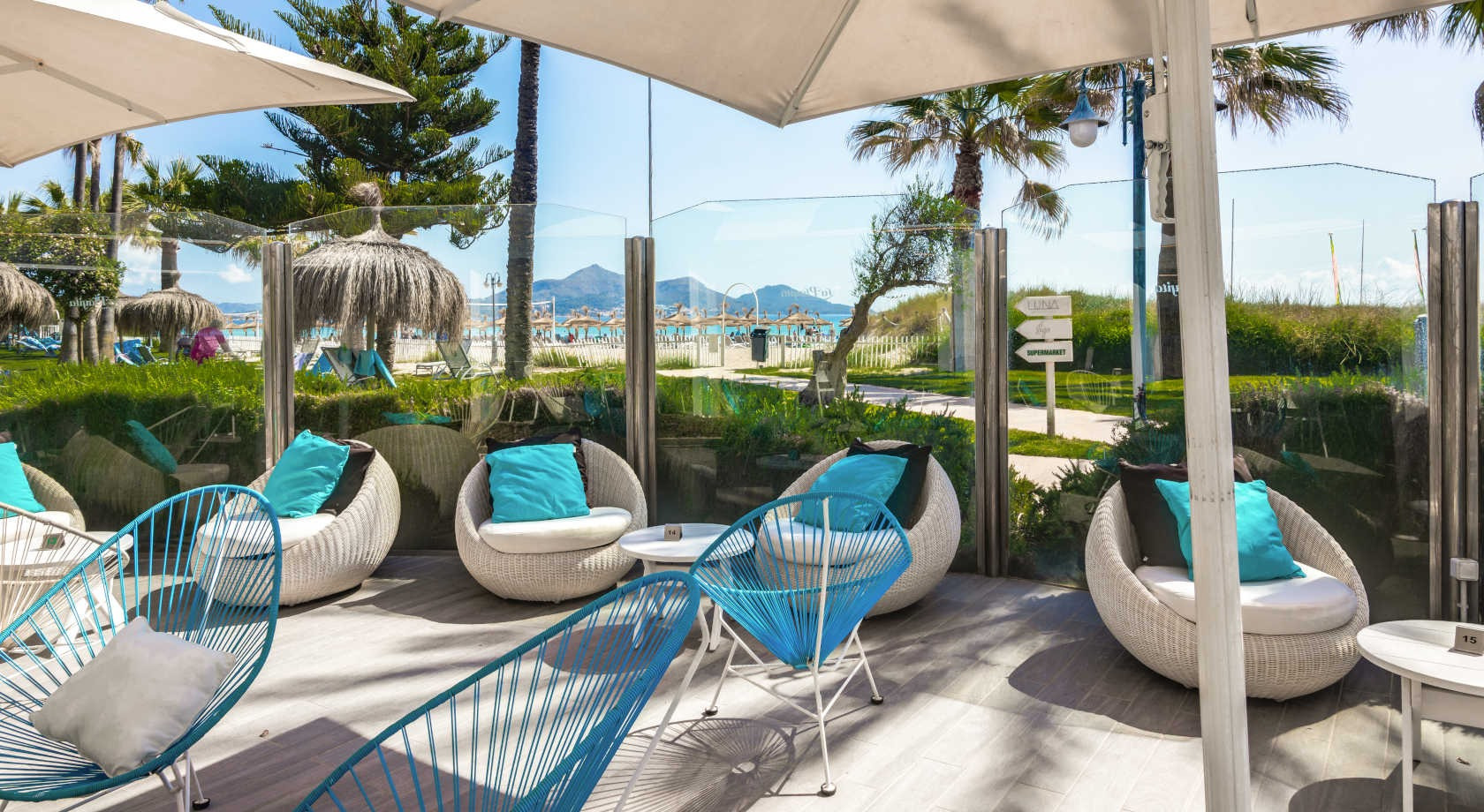 Terraza del hotel con sillas de mimbre y cojines turquesa frente al mar, ideal para Playa Esperanza Resort.