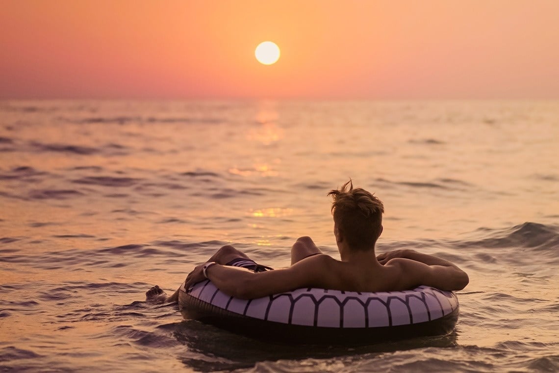 un hombre flota en un anillo inflable en el océano al atardecer