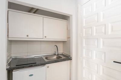 una pequeña cocina con gabinetes blancos y un fregadero de acero inoxidable