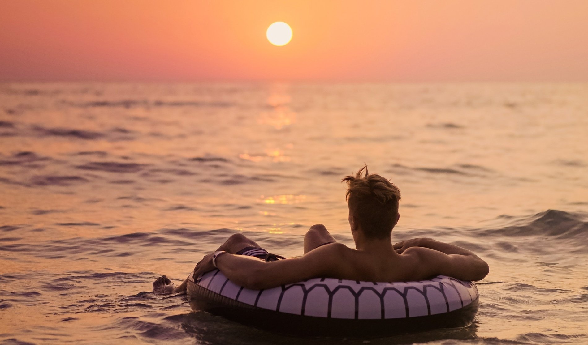 un hombre flota en un anillo inflable en el océano al atardecer