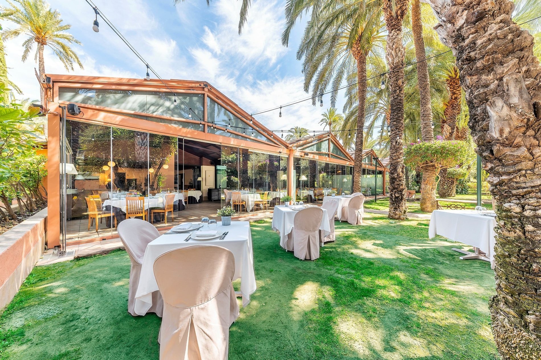 tables and chairs outside of a restaurant with palm trees in the background