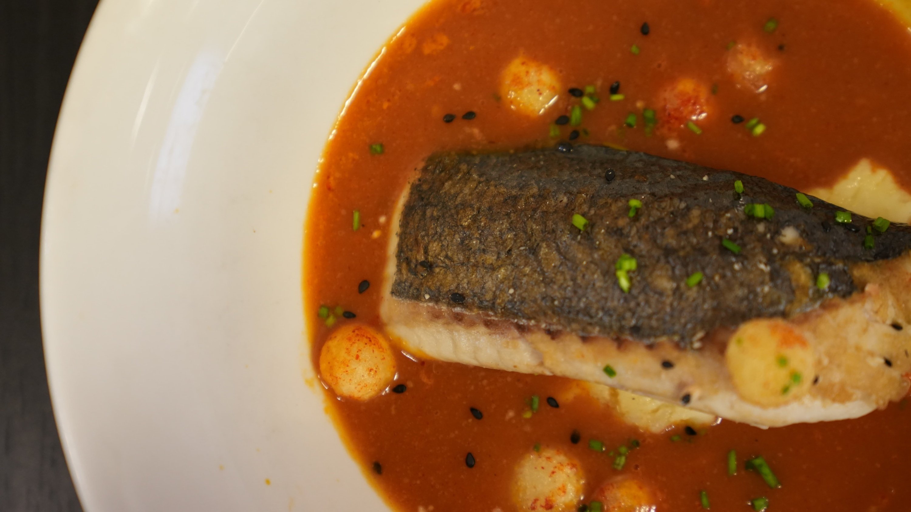 a white plate topped with a piece of fish in a sauce