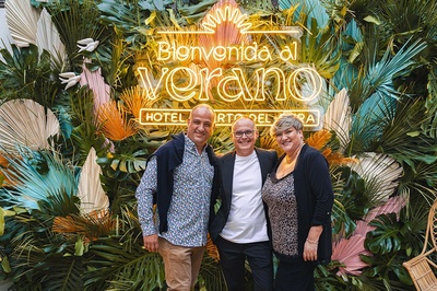 three people pose in front of a sign that says bienvenido al verano - 