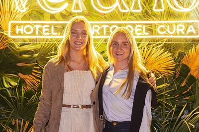 two women pose in front of a neon sign that says hotel - 