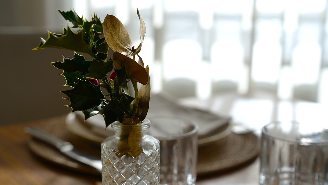 a glass vase filled with holly and leaves sits on a table