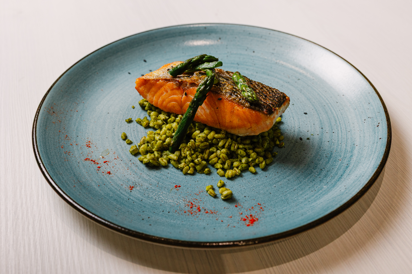 Pan-seared salmon with green grains & asparagus on a blue plate. Gourmet hotel restaurant meal.
