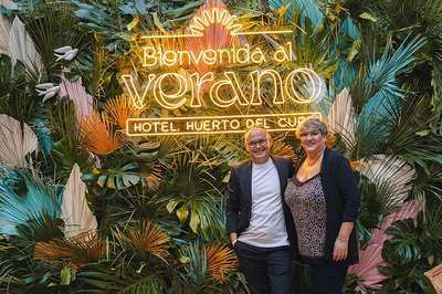 a man and woman stand in front of a sign that says bienvenido al verano - 
