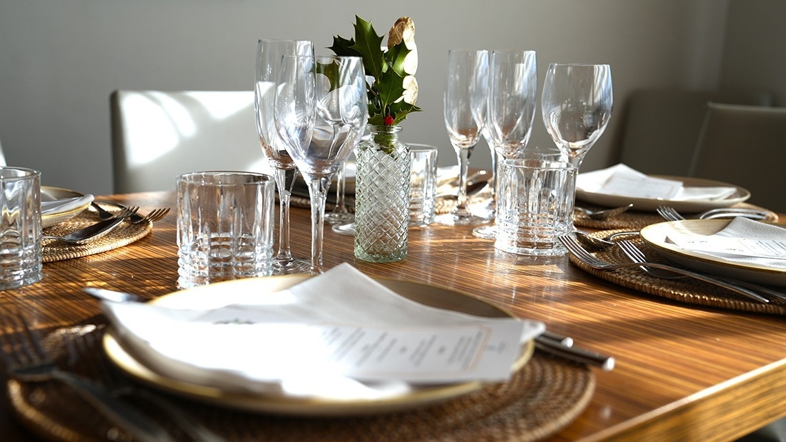 a table set with plates glasses and a vase with holly in it