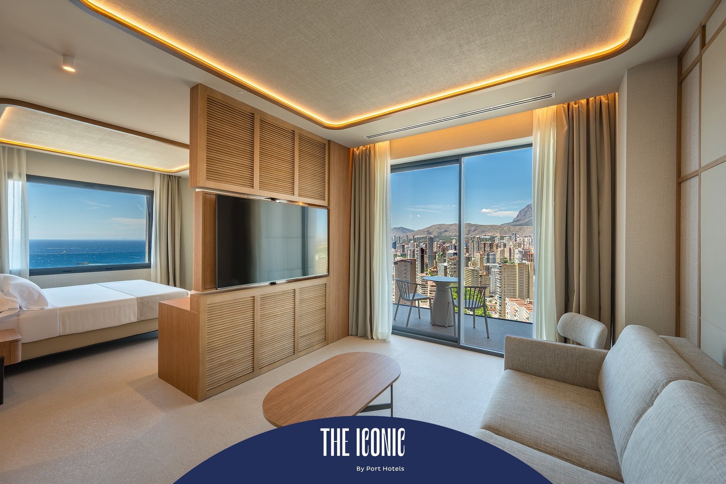 Habitación moderna con vista al mar y ciudad, TV, balcón y sofá, ideal para tu Port Hotels: Corporativa.