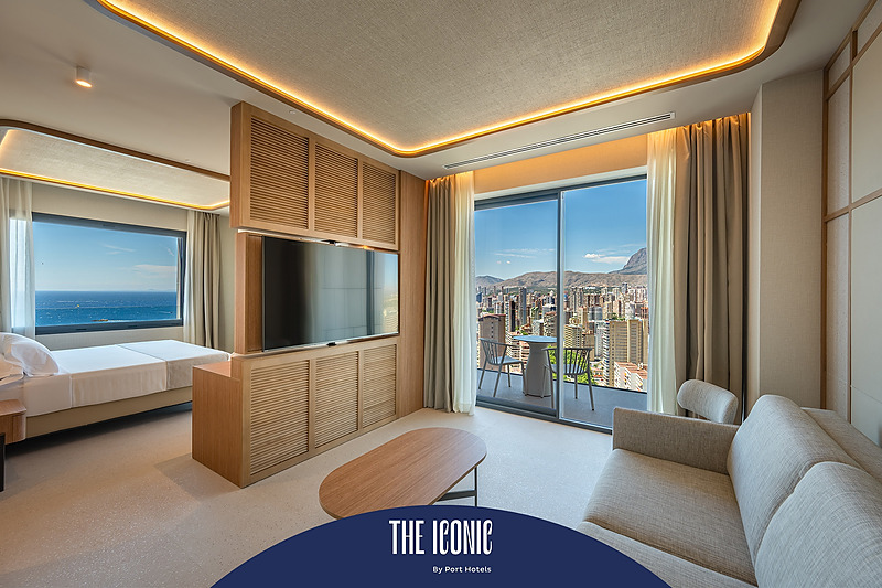 Habitación moderna con vista al mar y ciudad, TV, balcón y sofá, ideal para tu Port Hotels: Corporativa.