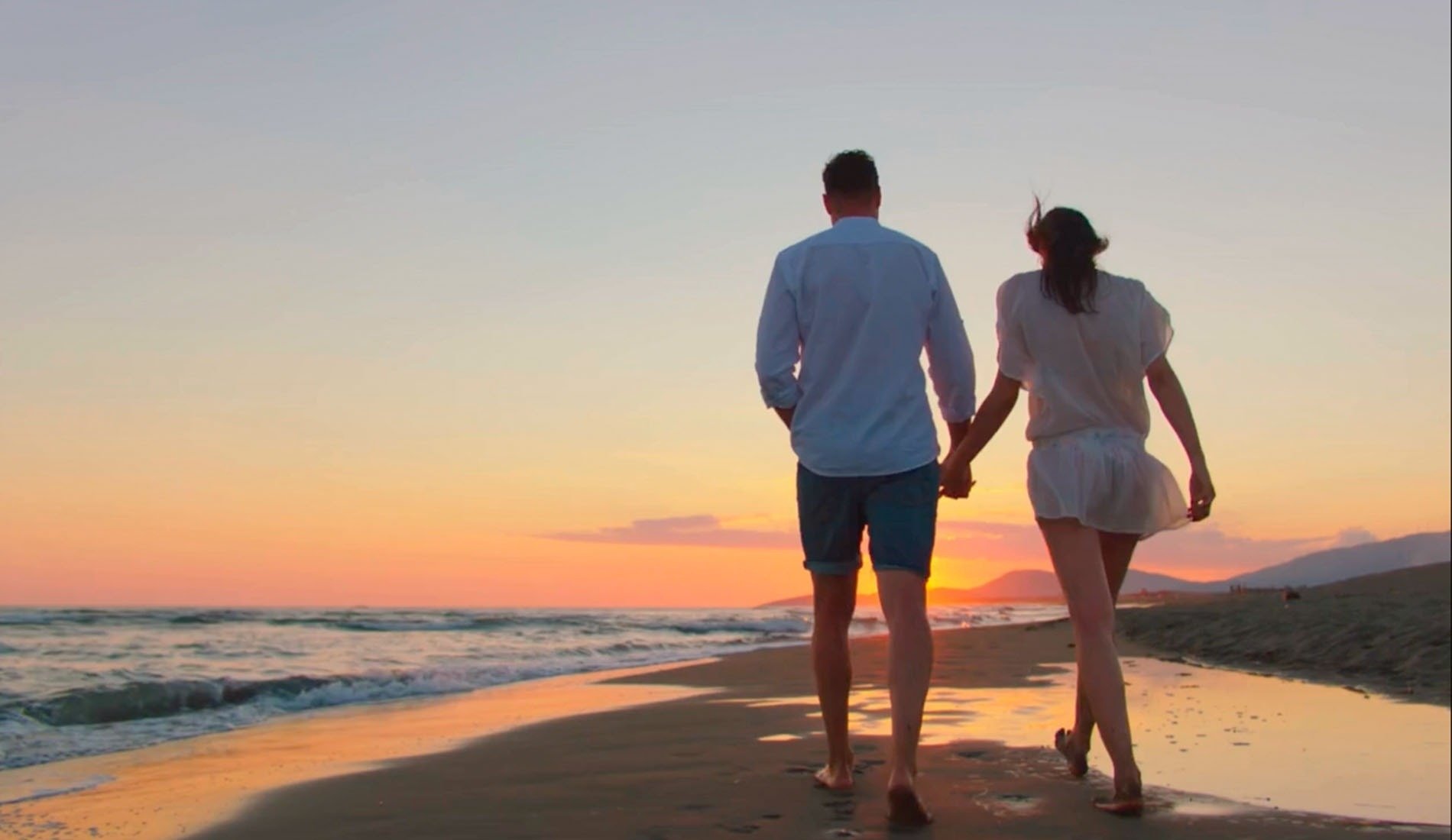 un hombre y una mujer sostienen las manos mientras caminan por la playa al atardecer