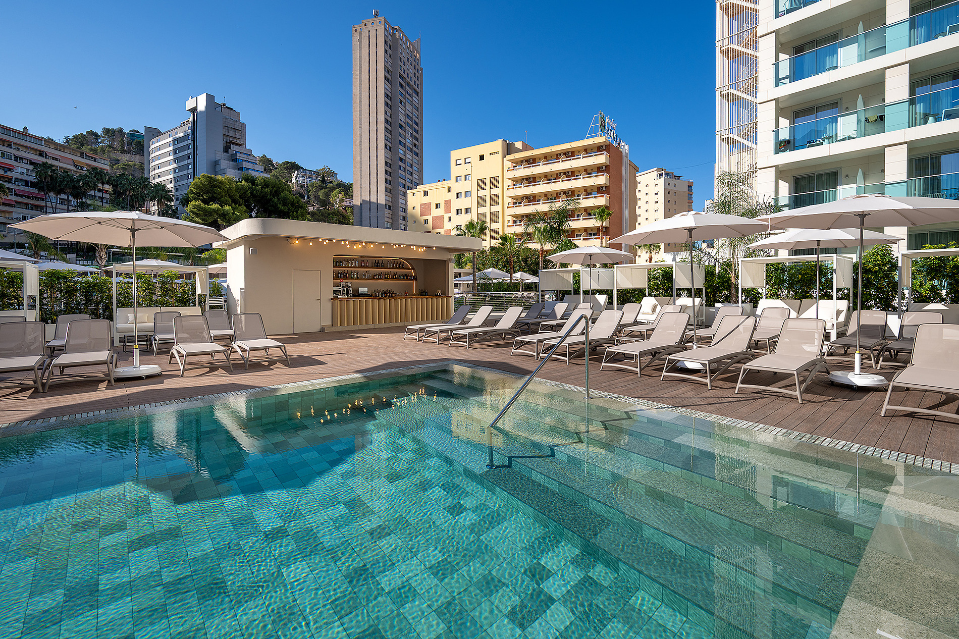 Piscina y tumbonas de hotel, un bar y edificios urbanos Port Benidorm Hotel & Spa | Alicante | Port Hotels | Web oficial.