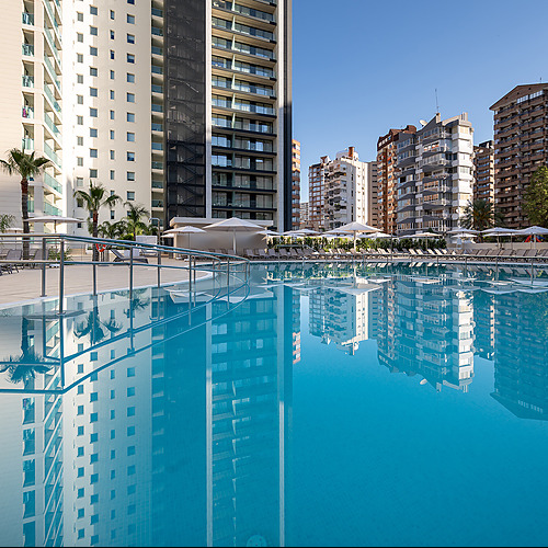 Reflejo de hoteles y palmeras en piscina azul, ideal para Port Hotels: Corporativa.