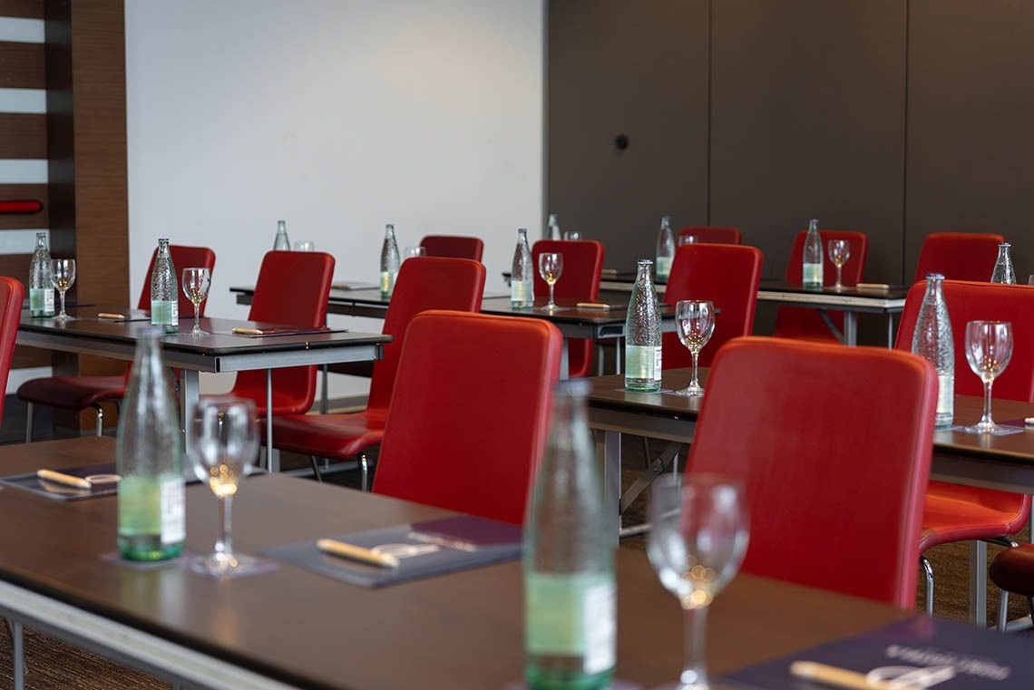 una sala de conferencias con mesas y sillas rojas y botellas de agua
