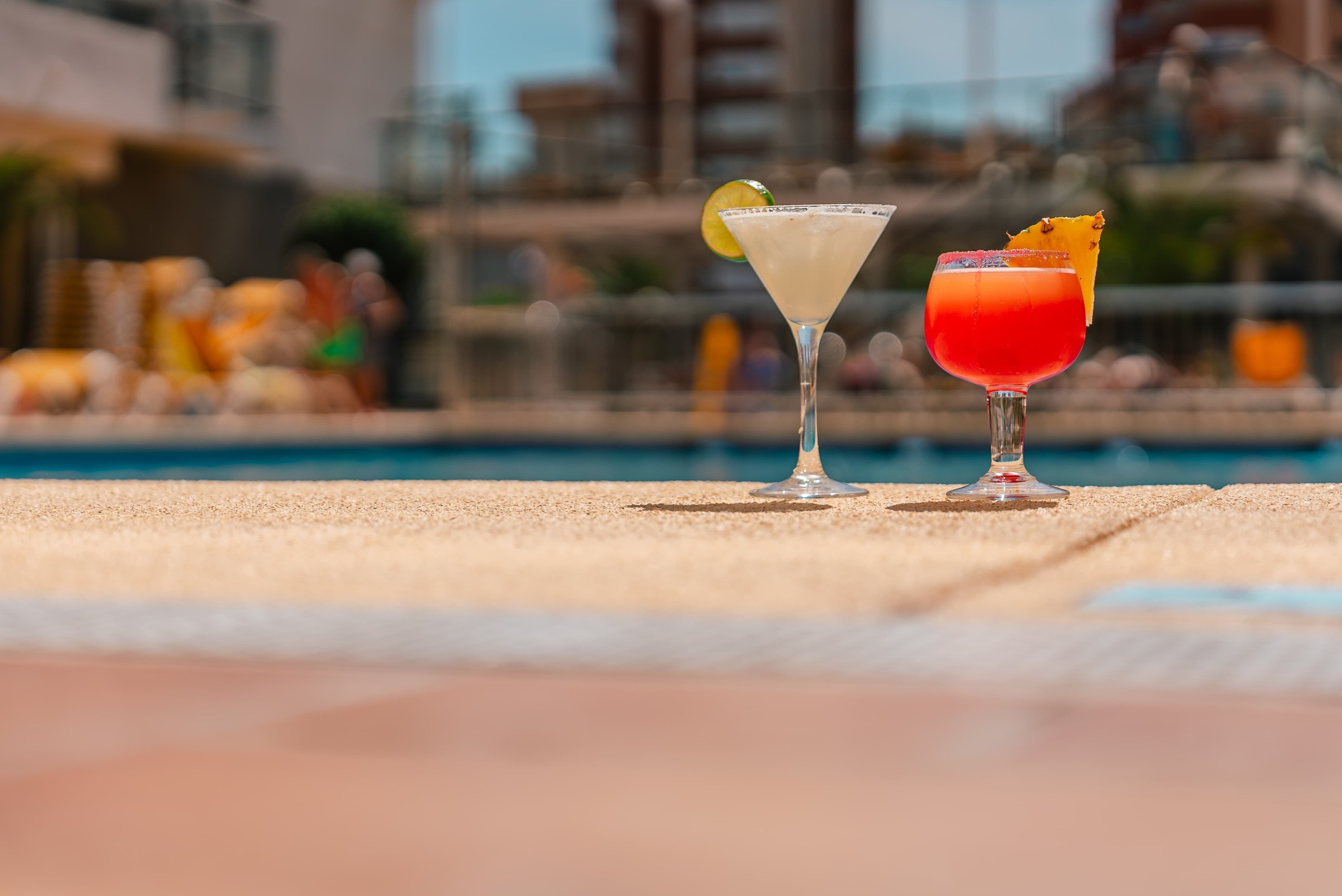 two drinks are on the edge of a swimming pool