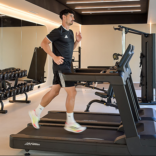 Hombre corriendo en cinta de gimnasio del hotel. Port Hotels: Corporativa, pesas y espejos.