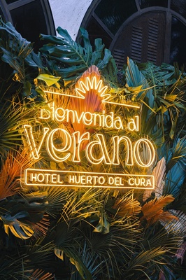 a neon sign that says bienvenido al verano hotel huerto del cura - 