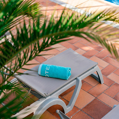 Toalha turquesa com logótipo Port Hotels: Corporativa numa espreguiçadeira junto à piscina.
