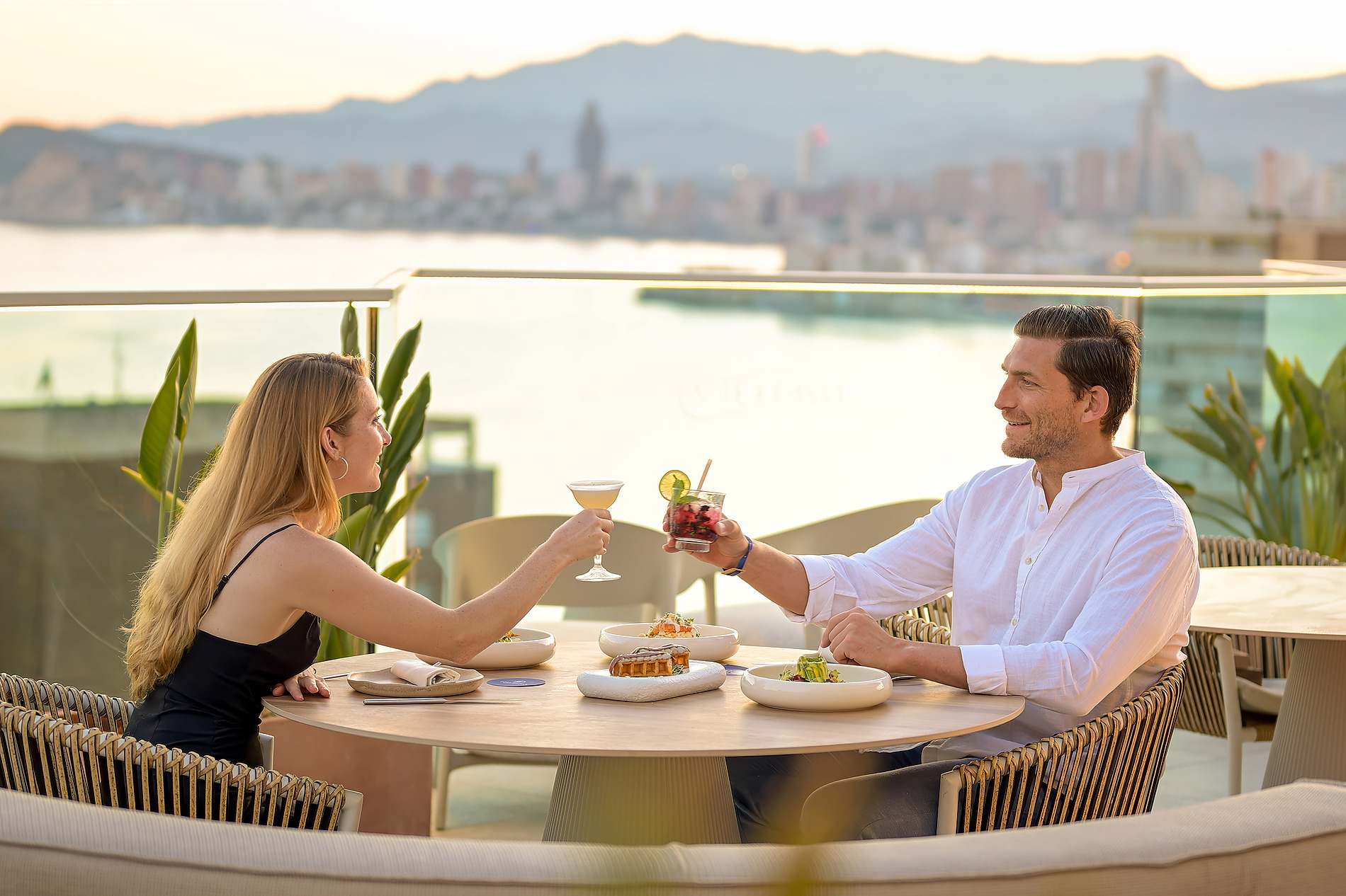 Pareja brindando en terraza de hotel con vista al mar y ciudad, cena romántica Port Benidorm Hotel & Spa | Alicante | Port Hotels | Web oficial.