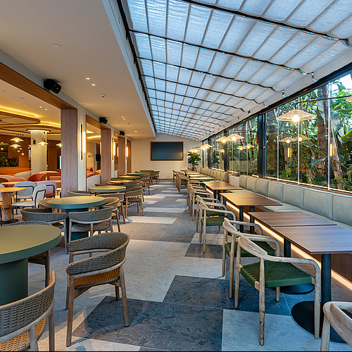 Comedor de hotel con mesas y sillas de madera junto a ventanales y vegetación Port Hotels: Corporativa.