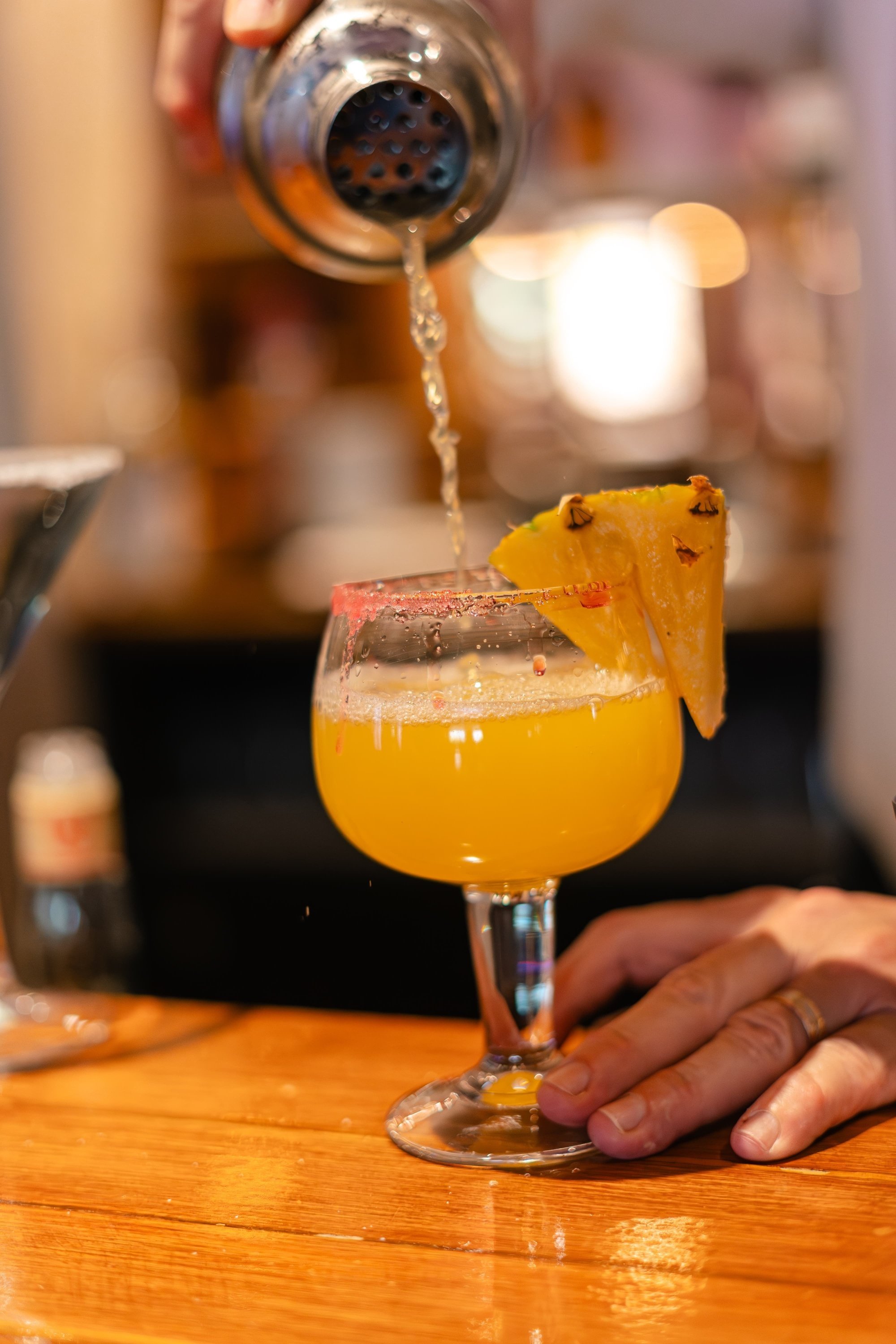 a person pouring a drink into a glass with a pineapple slice on top