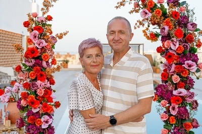 a man and woman standing in front of a floral arch - 