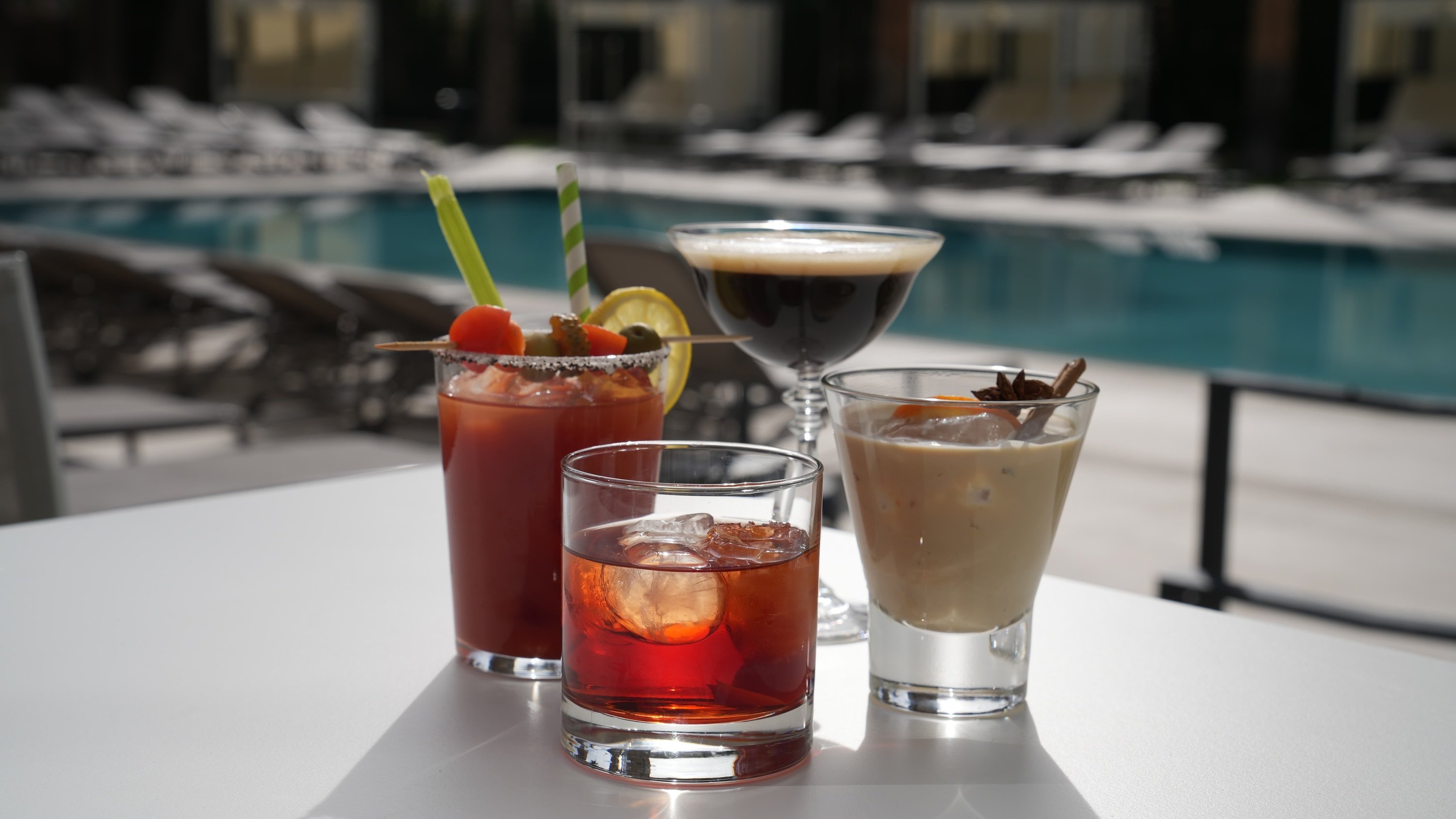 three drinks on a table with a pool in the background