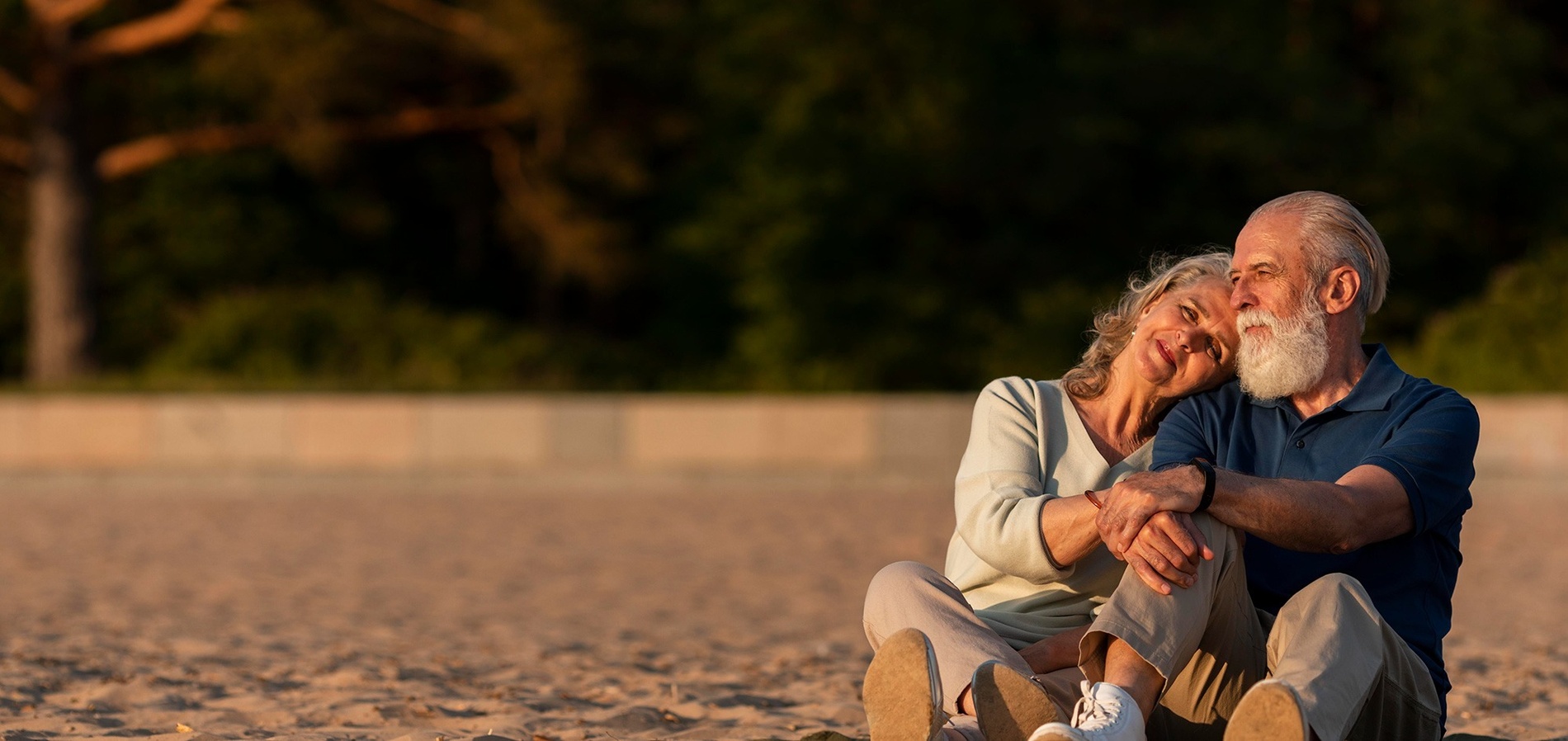 an elderly couple sitting on the beach with their arms around each other